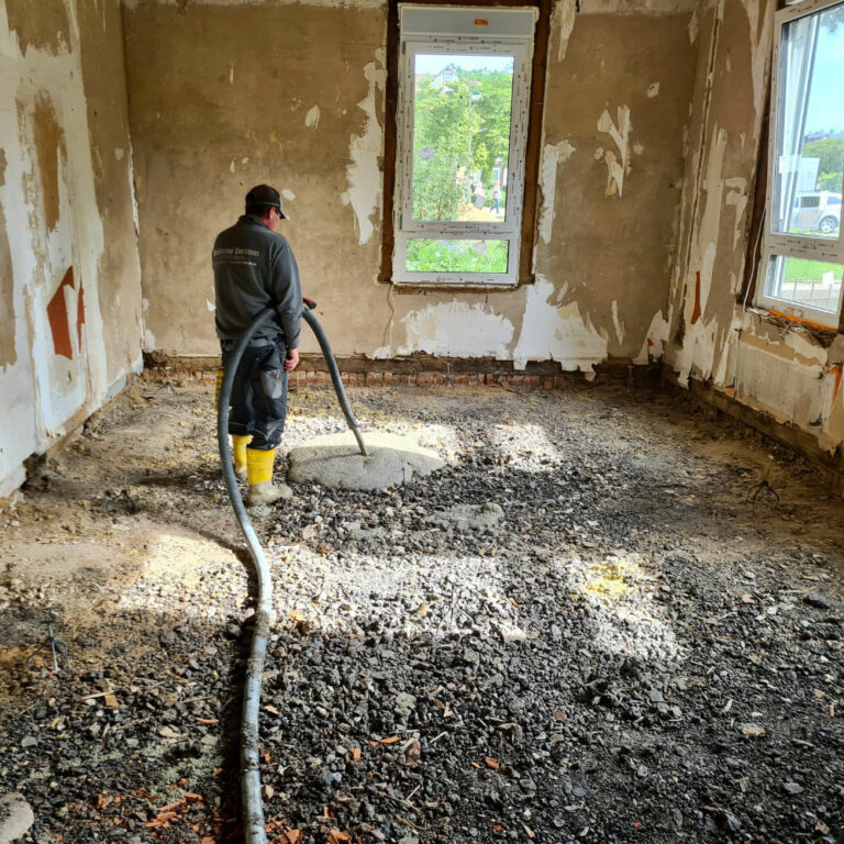 Derksen Estrichbau Mitarbeiter verlegt Flüssigdämmung in einem Altbau mithilfe eines Schlauchs, welcher frisch hergestellte Dämmung liefert